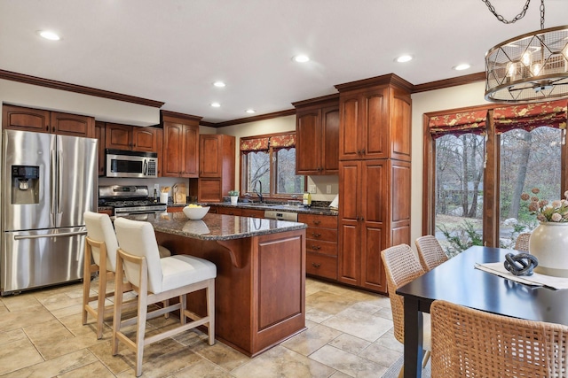 kitchen featuring a center island, sink, dark stone countertops, ornamental molding, and appliances with stainless steel finishes