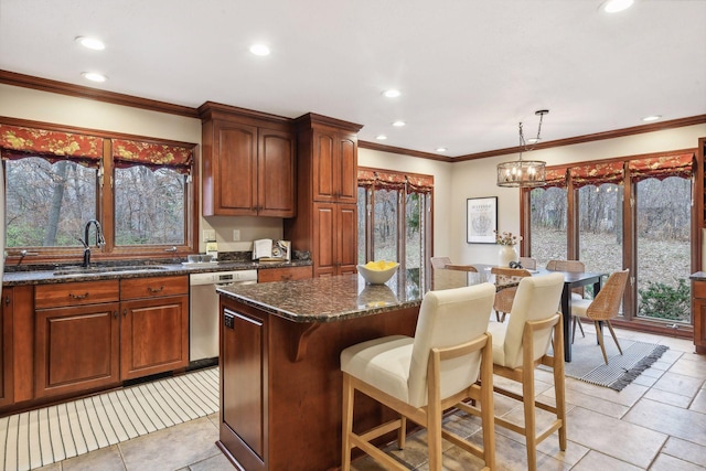 kitchen featuring stainless steel dishwasher, dark stone counters, sink, decorative light fixtures, and a kitchen island