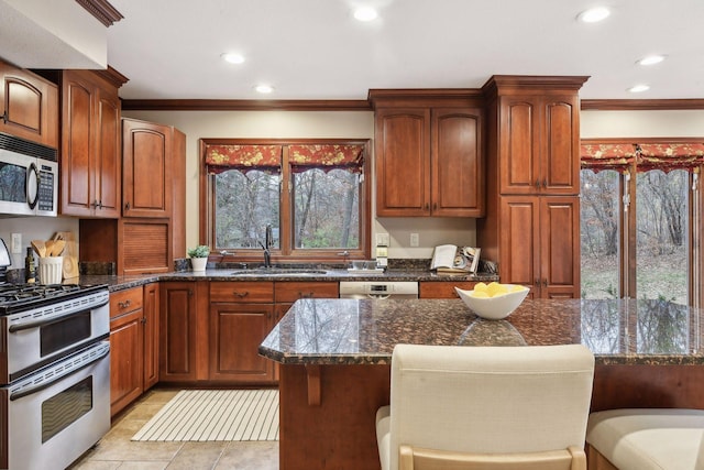 kitchen featuring appliances with stainless steel finishes, dark stone countertops, a breakfast bar area, and sink