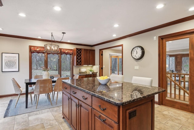 kitchen featuring a center island, crown molding, hanging light fixtures, and dark stone counters