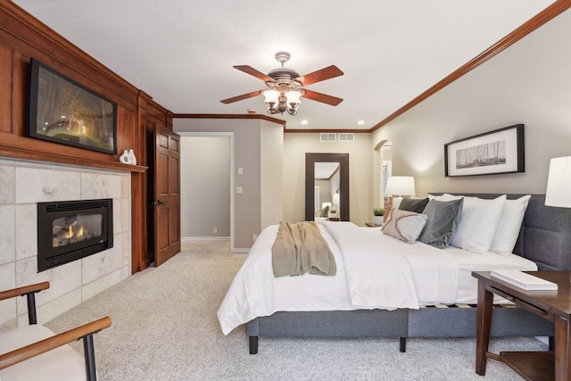 carpeted bedroom featuring a tiled fireplace, ceiling fan, and crown molding