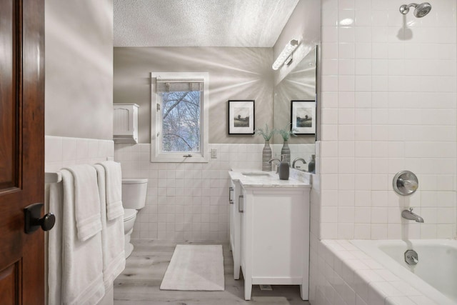 full bathroom with wood-type flooring, toilet, vanity, tile walls, and tiled shower / bath