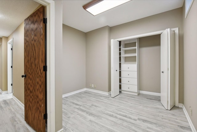 unfurnished bedroom with light wood-type flooring, a textured ceiling, and a closet