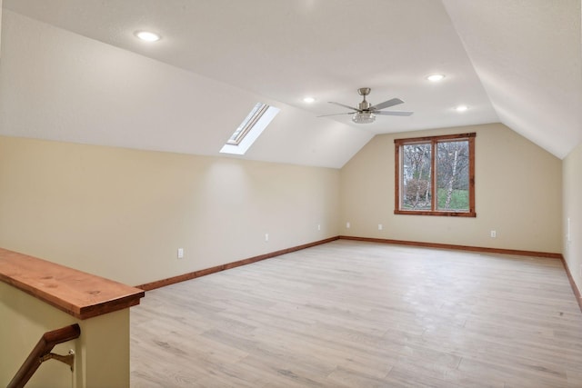 additional living space with vaulted ceiling with skylight, ceiling fan, and light hardwood / wood-style flooring