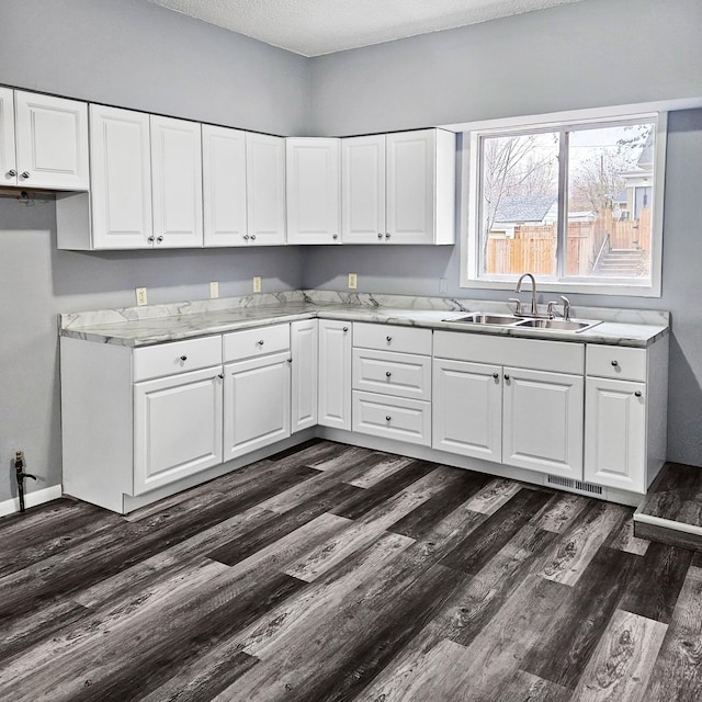 kitchen with light stone countertops, sink, dark hardwood / wood-style floors, a textured ceiling, and white cabinets