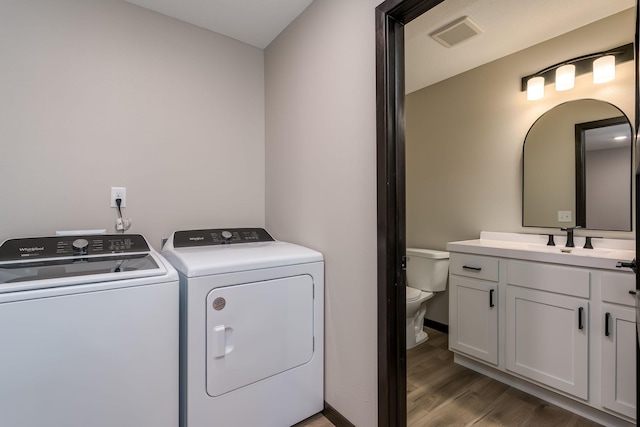 washroom featuring visible vents, baseboards, washing machine and dryer, wood finished floors, and a sink