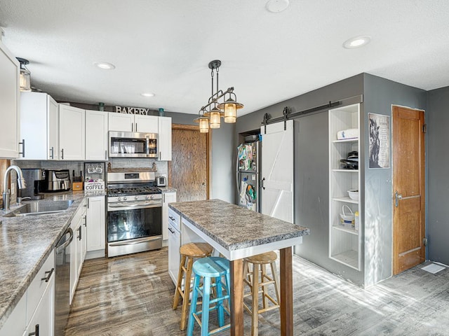 kitchen featuring sink, a barn door, a breakfast bar area, appliances with stainless steel finishes, and hardwood / wood-style flooring