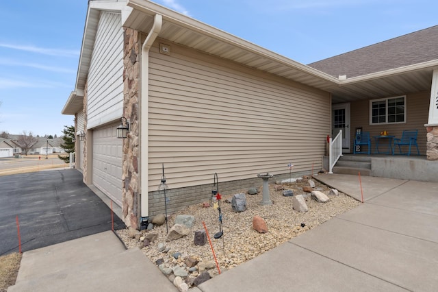 view of side of property featuring a garage, covered porch, aphalt driveway, and roof with shingles