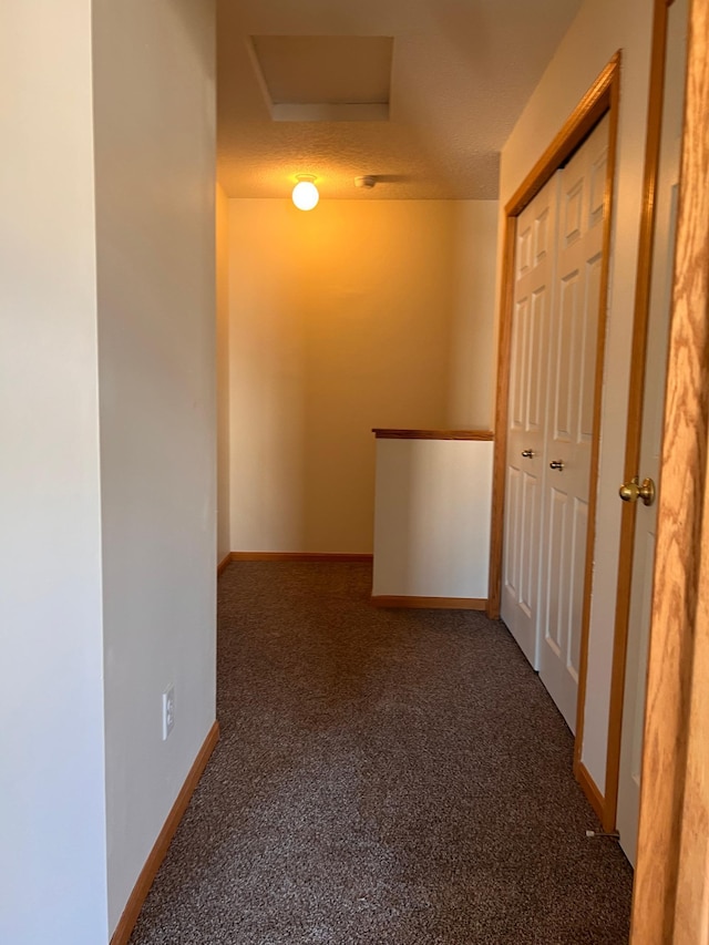 hallway with dark carpet and a textured ceiling