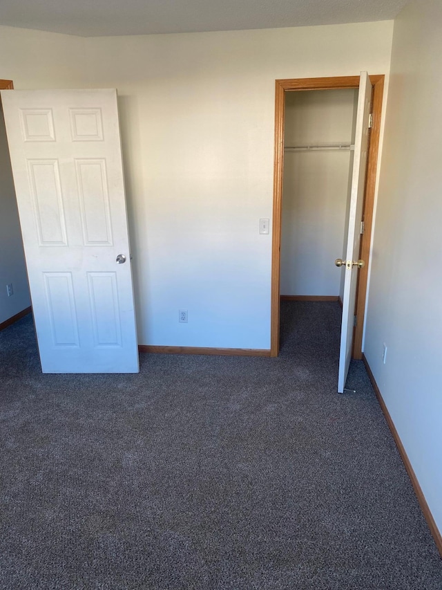 unfurnished bedroom with dark colored carpet and a closet