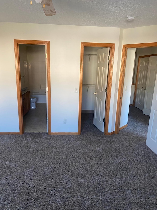 unfurnished bedroom with ensuite bath, a spacious closet, dark colored carpet, a textured ceiling, and a closet