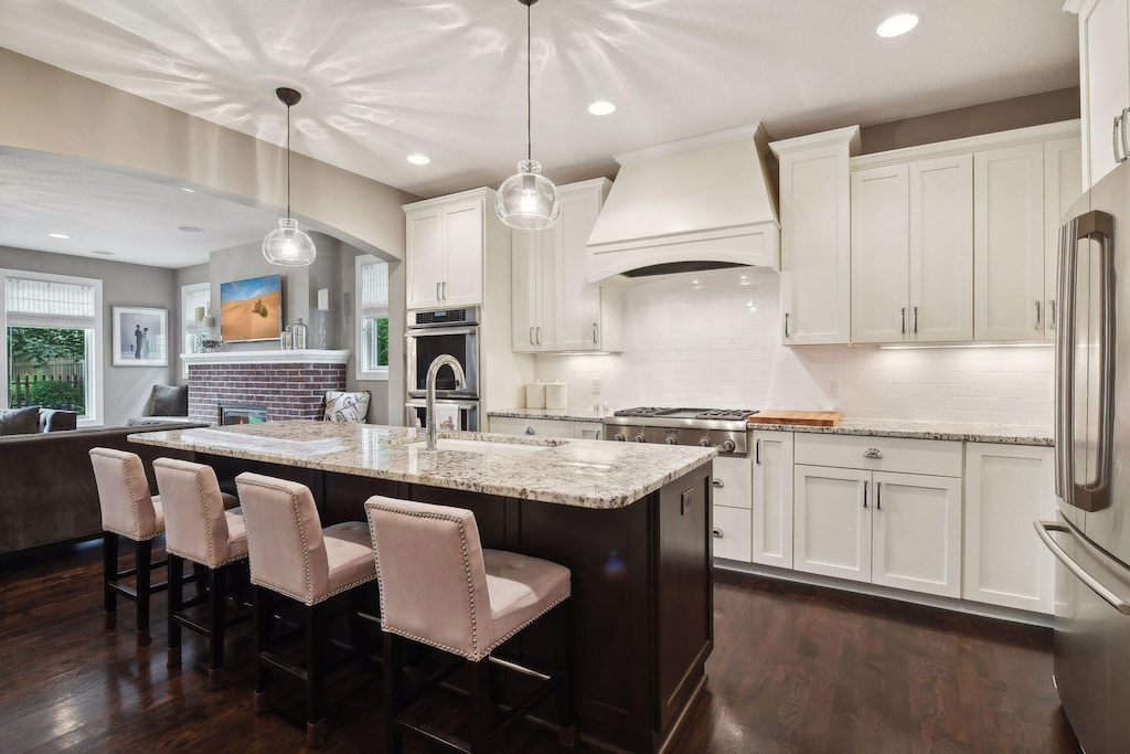 kitchen featuring custom range hood, stainless steel appliances, dark wood-type flooring, decorative light fixtures, and white cabinets