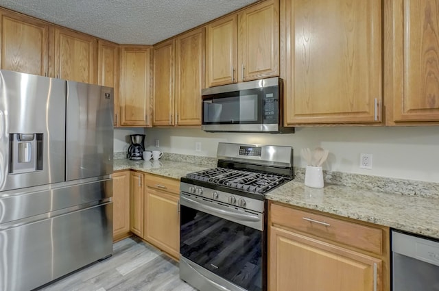 kitchen with light stone counters, light wood-type flooring, a textured ceiling, and appliances with stainless steel finishes