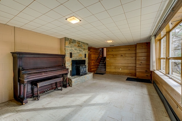 unfurnished living room with baseboard heating, a wood stove, and wood walls