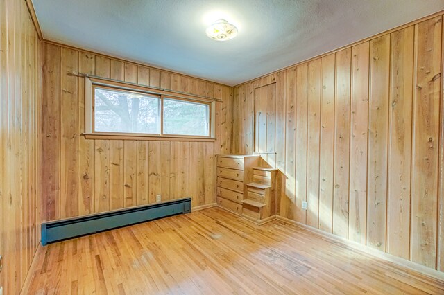 empty room featuring hardwood / wood-style floors, wood walls, and a baseboard radiator