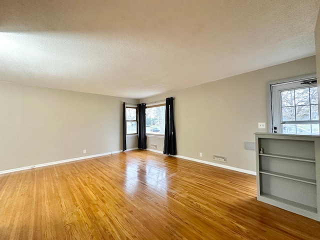 empty room featuring wood-type flooring, a textured ceiling, and a healthy amount of sunlight