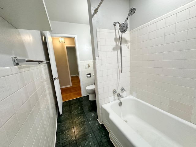 bathroom featuring tiled shower / bath, toilet, and tile walls