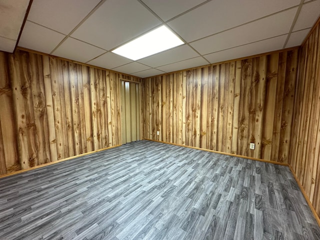 basement featuring a drop ceiling, dark wood-type flooring, and wooden walls