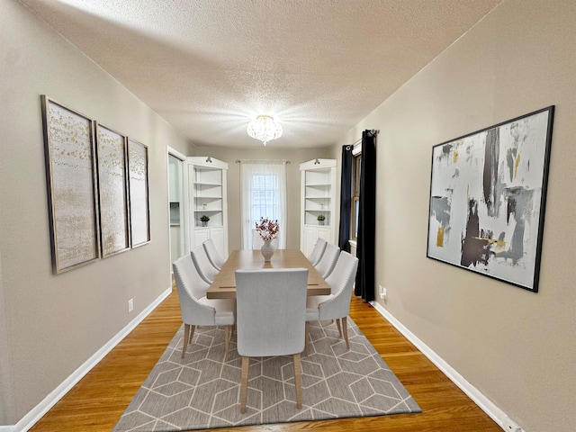 dining space with a notable chandelier, built in features, a textured ceiling, and hardwood / wood-style flooring