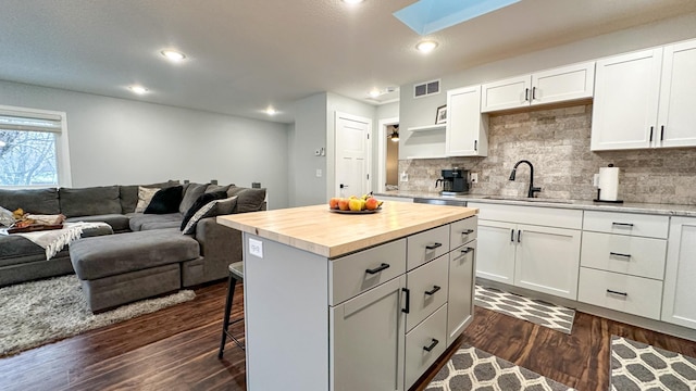 kitchen featuring sink, dark wood-type flooring, butcher block counters, white cabinetry, and a center island