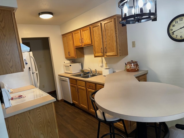 kitchen with white appliances, sink, dark hardwood / wood-style floors, a notable chandelier, and kitchen peninsula