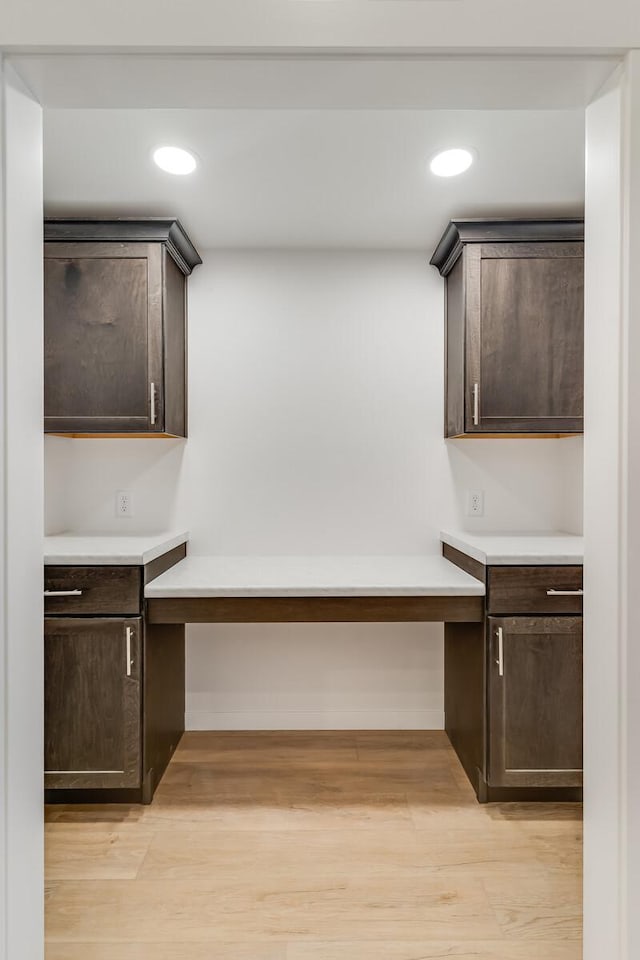 kitchen featuring light wood finished floors, built in study area, and dark brown cabinetry