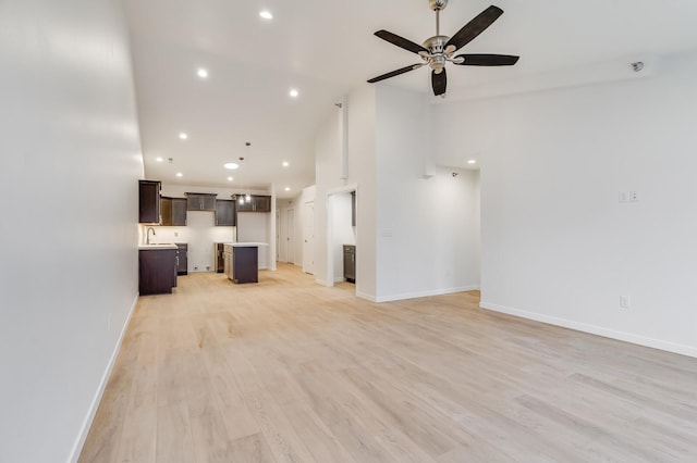 unfurnished living room featuring high vaulted ceiling, light wood-style floors, baseboards, and a sink