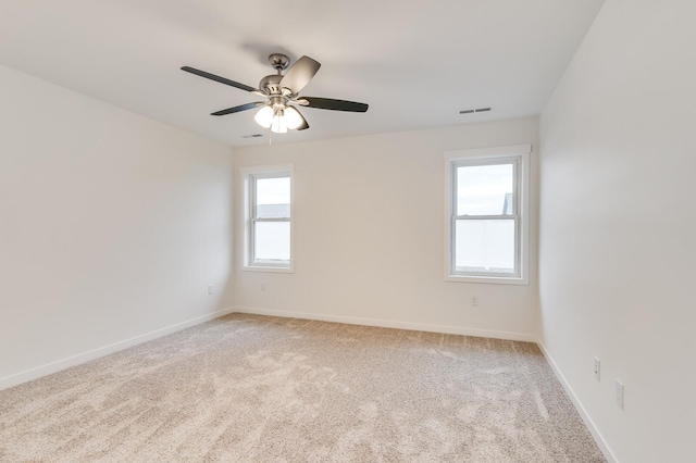 spare room featuring light carpet, ceiling fan, visible vents, and baseboards