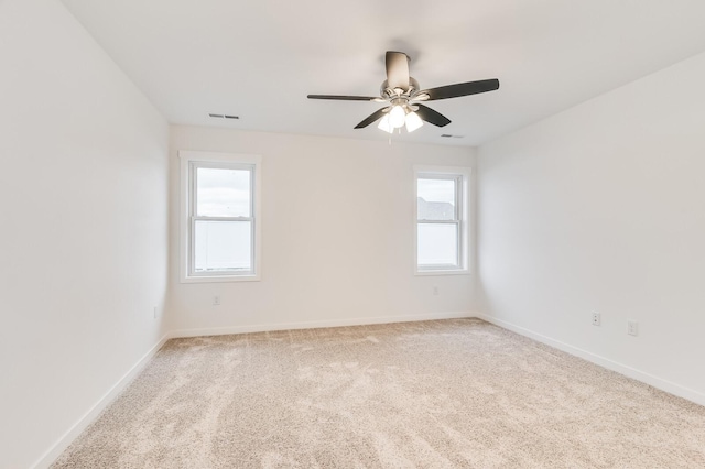 spare room featuring visible vents, baseboards, a wealth of natural light, and light colored carpet