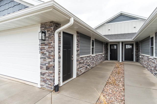 property entrance with an attached garage, stone siding, and board and batten siding