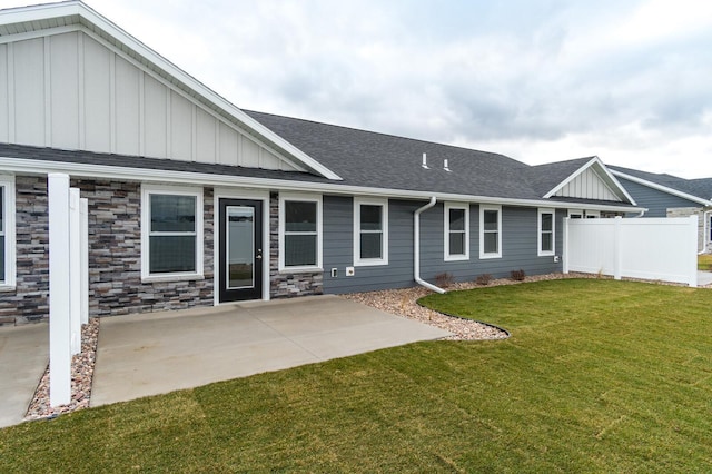 back of property featuring a shingled roof, a lawn, fence, a patio area, and board and batten siding