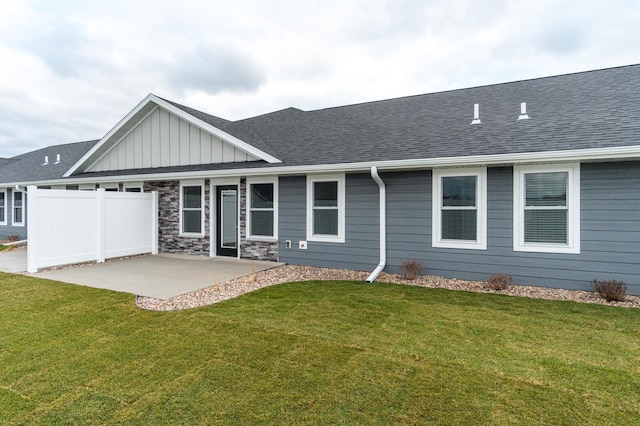 back of property with roof with shingles, a lawn, and a patio area