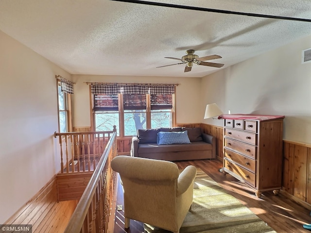 living area featuring an upstairs landing, a ceiling fan, wood walls, wainscoting, and wood finished floors