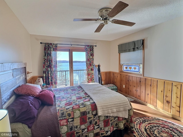 bedroom with access to exterior, a ceiling fan, wood walls, wainscoting, and wood finished floors