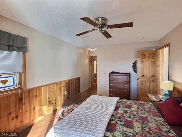 bedroom with wooden walls, ceiling fan, wainscoting, and wood finished floors