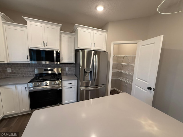 kitchen featuring decorative backsplash, a textured ceiling, stainless steel appliances, dark wood-type flooring, and white cabinets