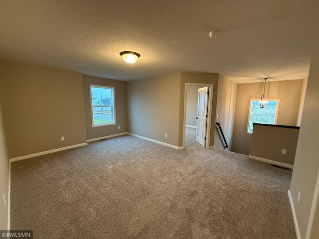 carpeted empty room with a textured ceiling and a chandelier