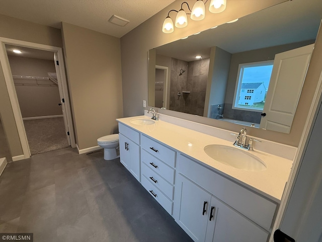 bathroom with concrete flooring, a textured ceiling, toilet, tiled shower, and vanity