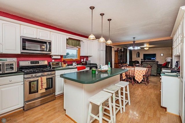 kitchen featuring hanging light fixtures, appliances with stainless steel finishes, a breakfast bar area, white cabinets, and light wood-type flooring