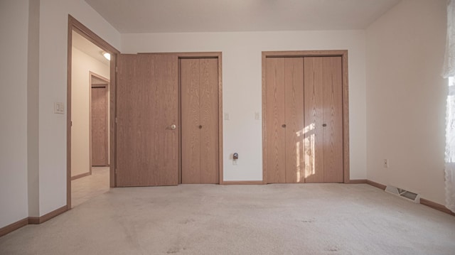 unfurnished bedroom featuring two closets and light colored carpet