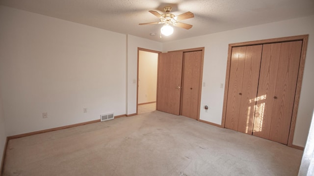 unfurnished bedroom featuring ceiling fan, a textured ceiling, light colored carpet, and multiple closets