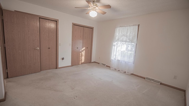 unfurnished bedroom featuring multiple closets, ceiling fan, light colored carpet, and a textured ceiling