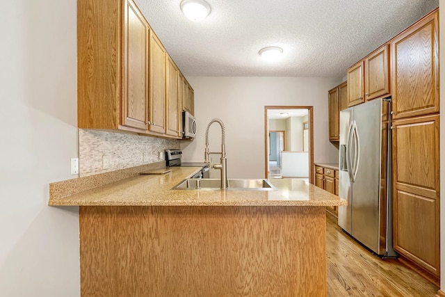 kitchen with sink, stainless steel appliances, kitchen peninsula, light hardwood / wood-style floors, and a textured ceiling