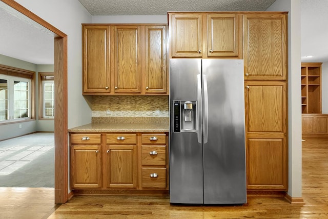 kitchen featuring stainless steel fridge with ice dispenser, a textured ceiling, tasteful backsplash, and light hardwood / wood-style flooring