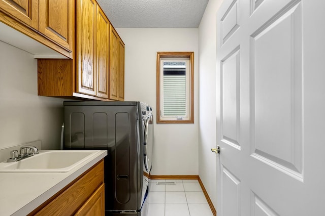 laundry room featuring sink, cabinets, a textured ceiling, washer and clothes dryer, and light tile patterned floors