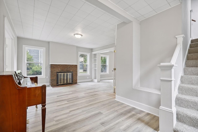 interior space with baseboards, stairway, light wood-type flooring, and a brick fireplace