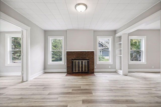 unfurnished living room featuring a brick fireplace, wood finished floors, and a healthy amount of sunlight