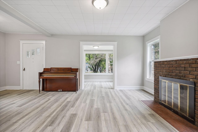 unfurnished living room featuring a brick fireplace, baseboards, a wealth of natural light, and wood finished floors