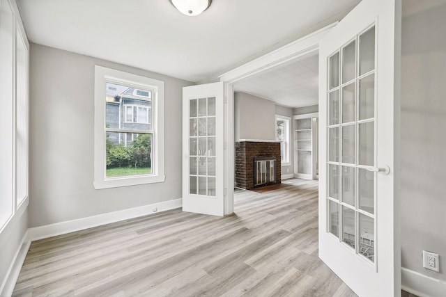 spare room featuring light wood-style floors, a brick fireplace, french doors, and baseboards