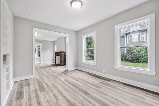 empty room with light wood-style floors, a fireplace, and baseboards